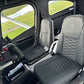 Black quilted aviation cockpit seats installed inside a Cessna C162 cabin, with the pilot's seat in front and a window view of green grass outside.